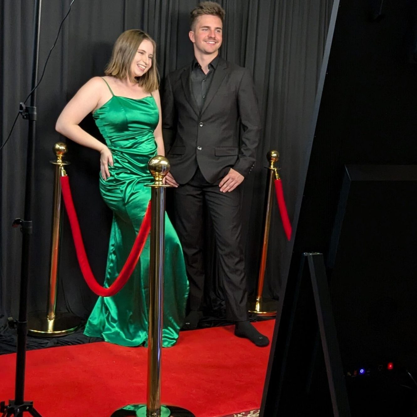 two people standing in front of a mirror photobooth in fancy clothes and standing on a red carpet